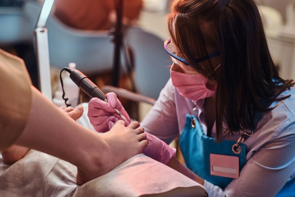 Young cheerful nail master is working on client's toe nails at her pedicure studio.